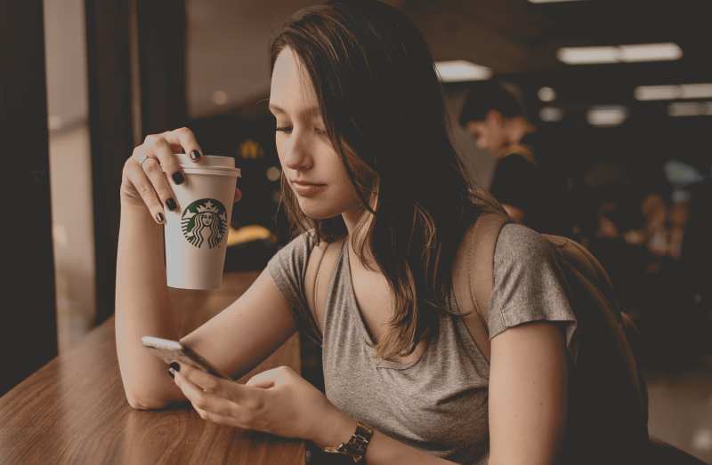 Giovane donna che messaggia mentre beve un caffè in una caffetteria 