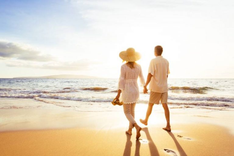 couple holding their hands while walking on the beach