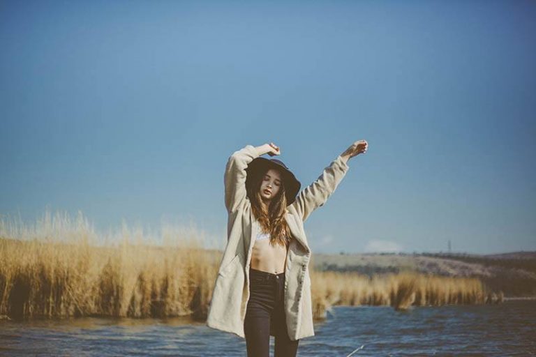 woman wearing hat standing outside and raising hands