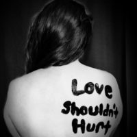 foto della schiena di una donna con la scritta "love should't hurt" (l'amore non deve far male)