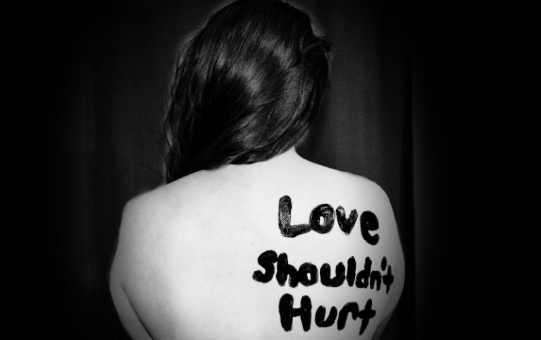 photo of woman's back with love shouldn't hurt written on it