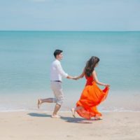 uomo e donna in abito arancione che camminano in riva al mare
