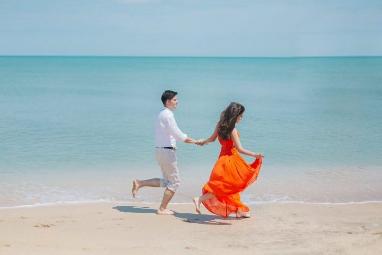 man and woman in orange dress walking beside sea