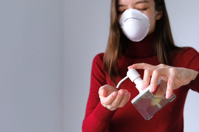 woman in red top applying sanitizer wearing n95 mask