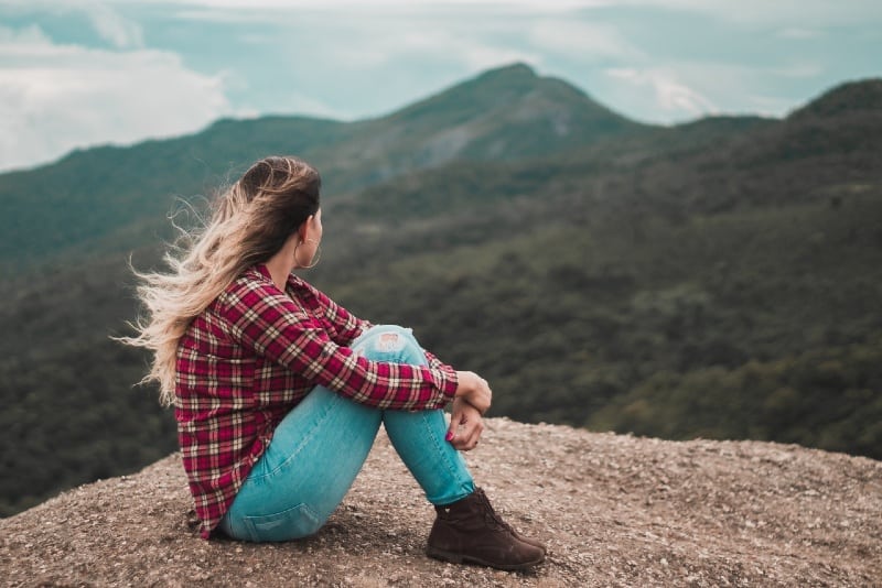woman sitting on rock and looking at mountain