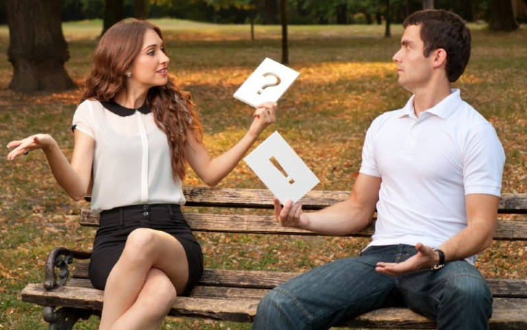 Woman with question mark sign near man with exaclamation mark sign sitting on a bench