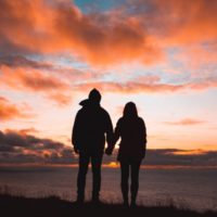 man and woman holding hands standing on cliff