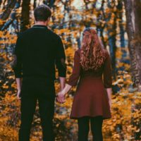 Vista traseira de um casal de mãos dadas em frente a uma floresta de outono