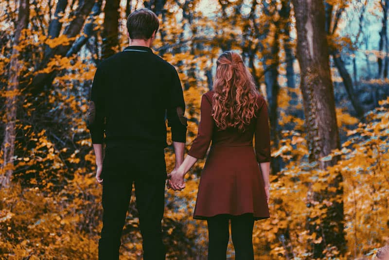 Vista trasera de una pareja cogida de la mano frente a un bosque otoñal