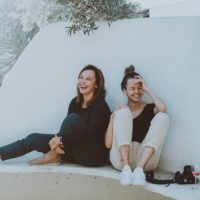 two laughing women sitting on white bench