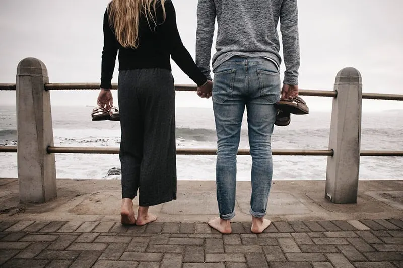 Backview of a couple's legs standing on wooden deck on sea