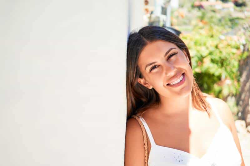 Hermosa chica apoyada en la pared blanca colgada amable