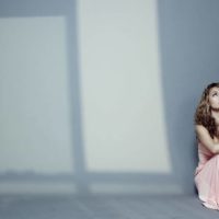 woman alone sitting on the floor wearing a beige dress with lights coming in from windows