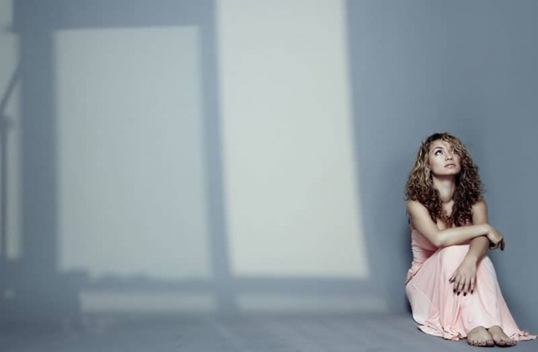 woman alone sitting on the floor wearing a beige dress with lights coming in from windows