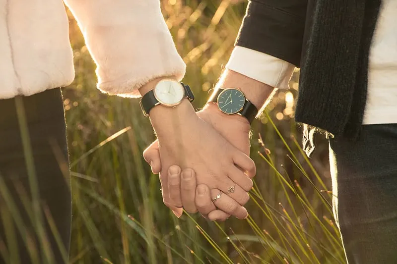 Close up of man woman's clasped hands wearing matching wristwatches