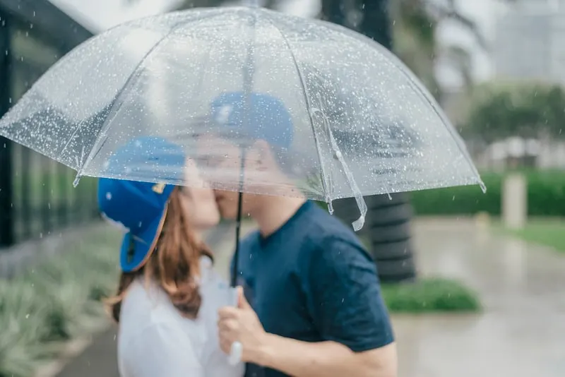 couple kissing under umbrella both in blue caps
