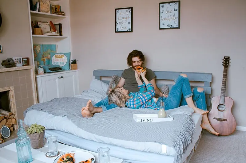 Couple in bed eating pizza