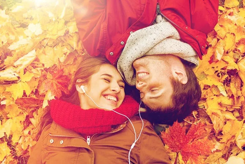 Couple sharing earphones while lying down on bed of autumn leaves