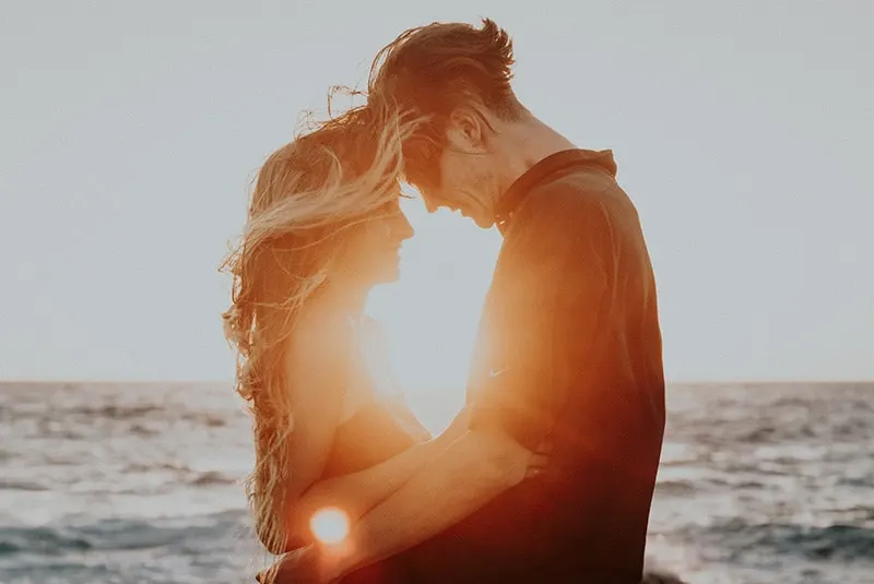 Embracing couple foreheads touching during sunset in front of the sea