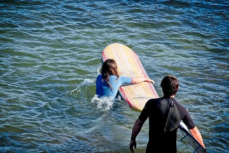 Couple surfing woman going out to open sea