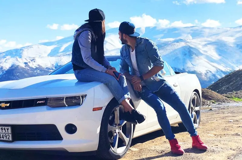 Couple leaning on white chevrolet coupe staring at mountains