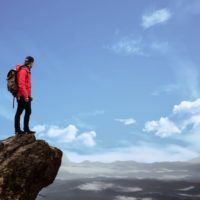man in red jacket standing on cliff
