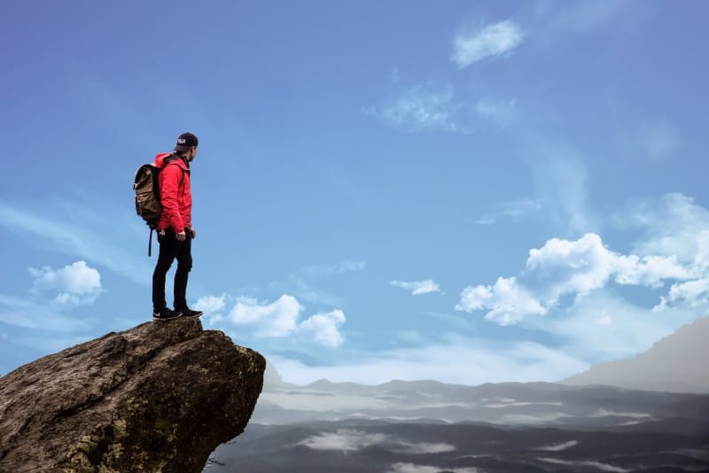 man in red jacket standing on cliff