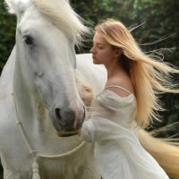 mujer vestida de blanco cerca de un caballo blanco