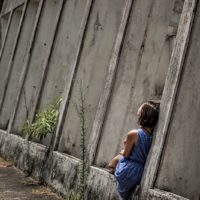 girl sitting alone beside concrete wall