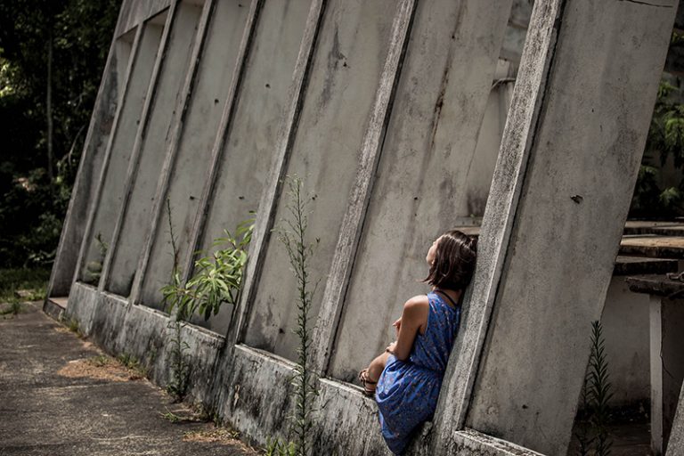 girl sitting alone beside concrete wall