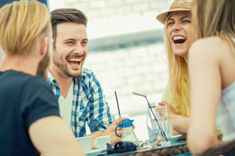 Os amigos sorriem e sentam-se num café, bebem café e divertem-se juntos