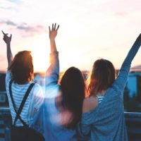 tres mujeres levantando las manos durante la puesta de sol