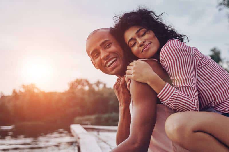 Giovane coppia felice che si abbraccia e sorride mentre è seduta vicino al lago