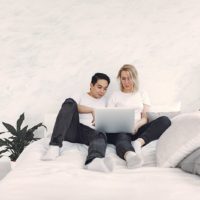 couple sitting on the bed while using laptop