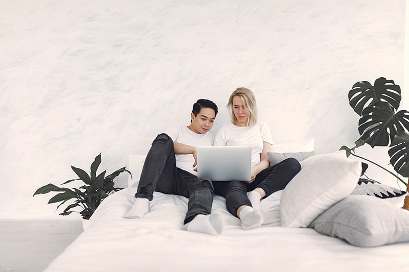 couple sitting on the bed while using laptop