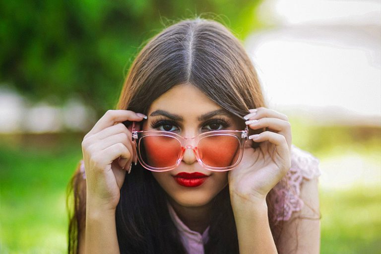 Lady wearing read tinted sunglasses propped on her elbows on the ground