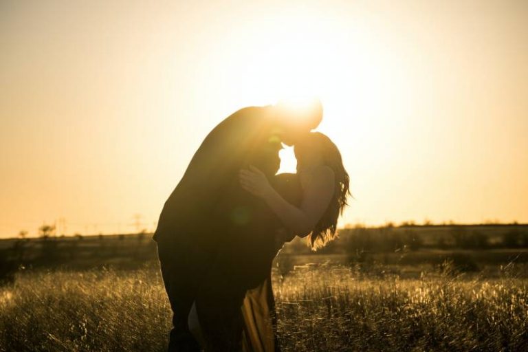 casal a beijar-se no exterior ao pôr do sol