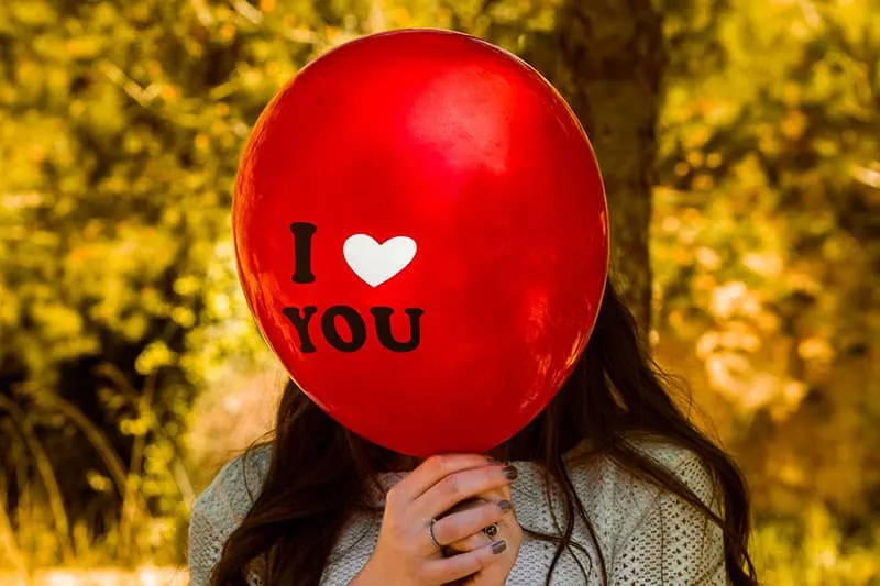 I Love You red balloon held in front covering woman's face