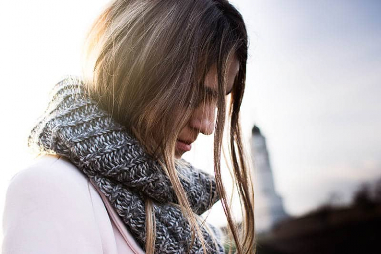 a sad woman with a scarf stands outside