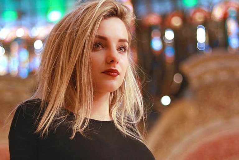 a blonde-haired woman stands and looks away