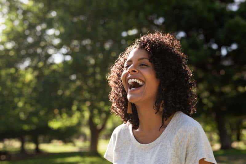 Laughing woman with curly hair while standing outside in a park