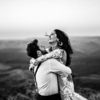 fotografia em tons de cinzento de um homem e uma mulher abraçados perto de uma colina