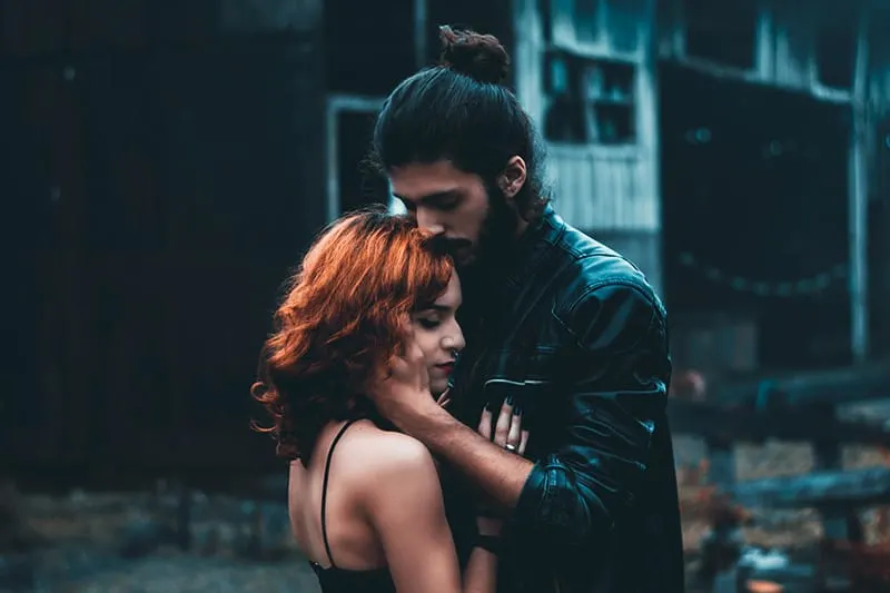 Man with hair in a bun holding woman by the chin