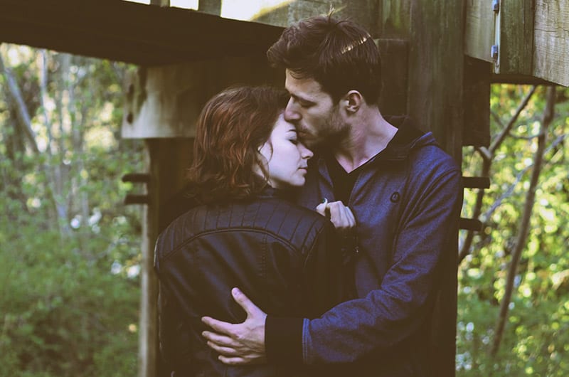 Un uomo abbraccia una donna e la bacia sulla fronte accanto a un ponte di legno