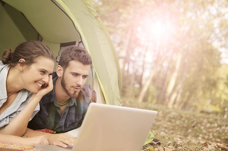 Man and woman sharing a laptop on the ground at tent opening outdoors