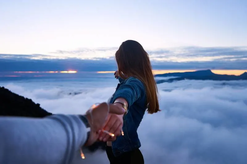 Person holding woman hand on top of hill