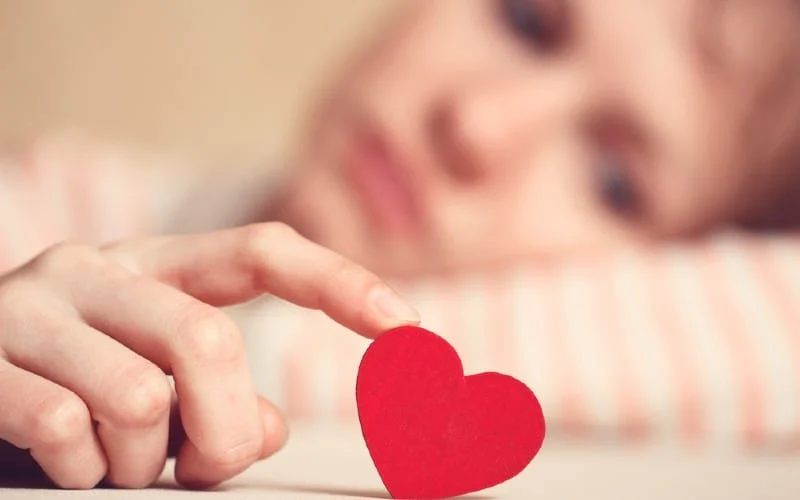Sad girl touching heart symbol with finger and looking at it