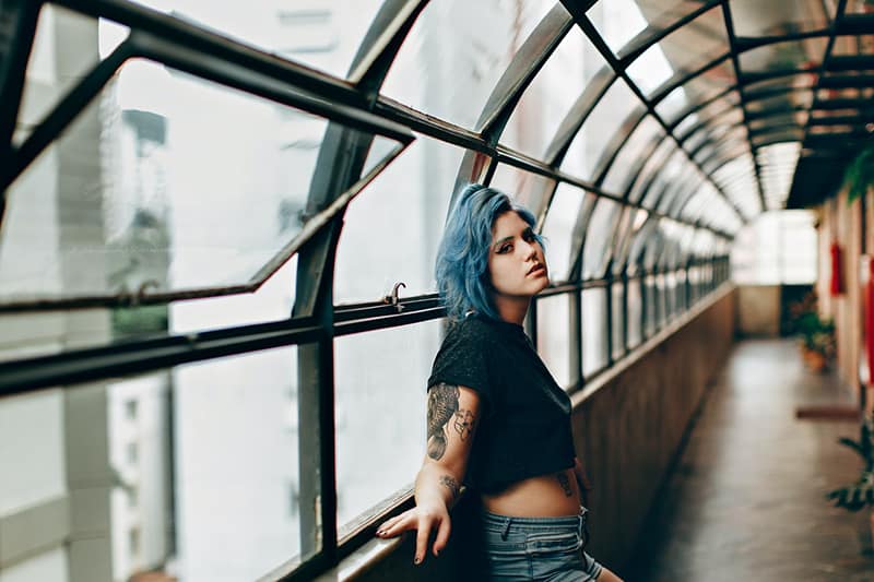 woman with blue hair standing in empty corridor