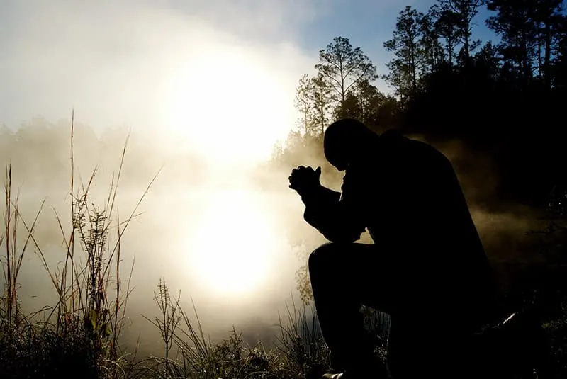 Silhouette of a man outdoors praying on bent knee