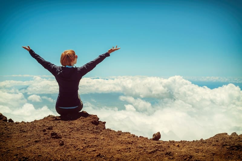 woman raising hands on a cliff